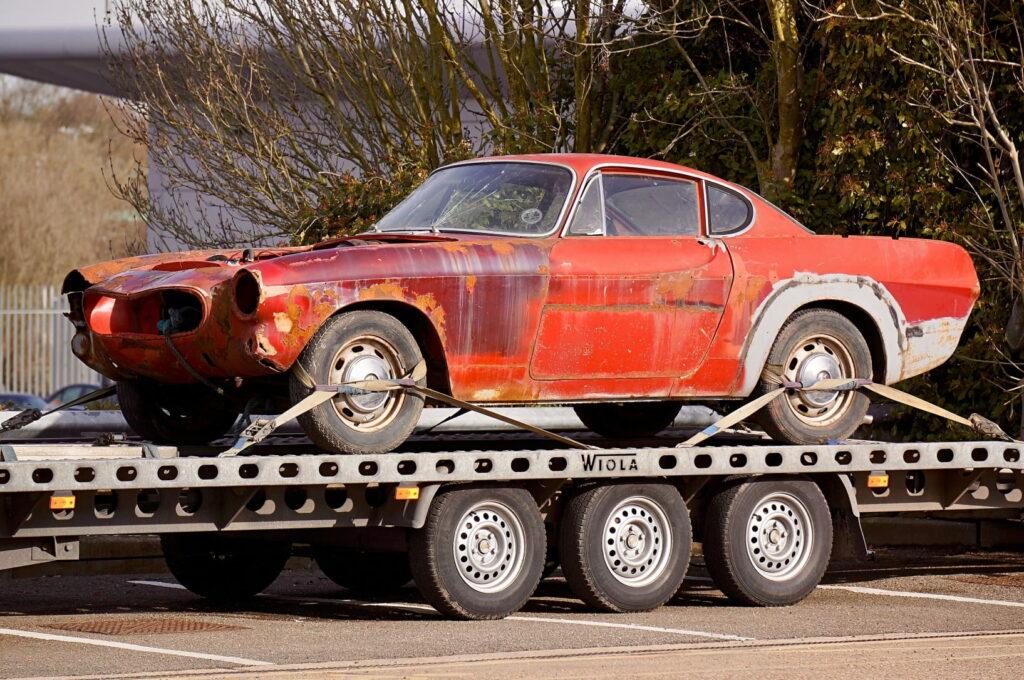Old abandoned car being towed with flatbed tow truck
